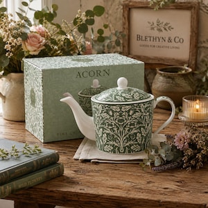 May include: A fine china teapot featuring a green and white acorn and leaf pattern, a matching lid with a white knob, and a curved spout. The teapot is displayed in front of its original green box labelled ACORN and FINE CHINA in white text.