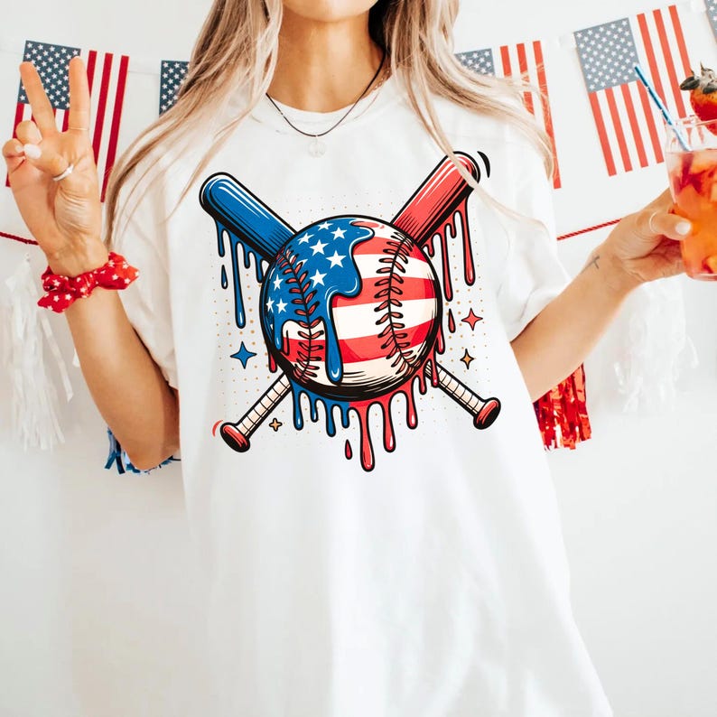 K&ouml;nnte beinhalten: Wei&szlig;es T-Shirt mit einem Baseball-Design, das die amerikanische Flagge enth&auml;lt, gekreuzt mit zwei Baseballschl&auml;gern. Der Baseball hat rote, wei&szlig;e und blaue Akzente mit einem tropfenden Farbeffekt. Die Schl&auml;ger sind blau und rot.