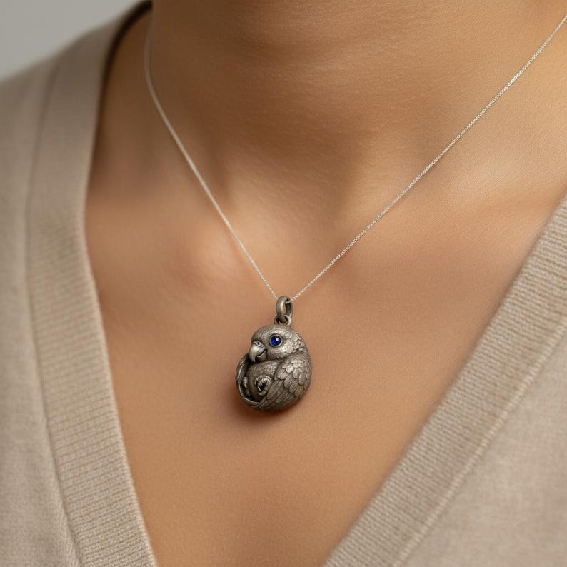 May include: A silver-colored pendant necklace featuring a detailed owl design. The owl pendant has a blue gemstone eye and is suspended from a delicate silver chain. The owl is in a curled position.