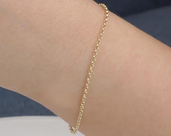 May include: A delicate gold bracelet with a chain-link design. The bracelet is a warm yellow color and appears to be made of metal. The bracelet is worn on a person's wrist.