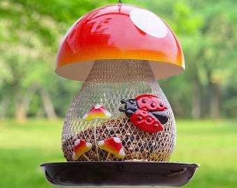 May include: A whimsical mushroom-shaped bird feeder with a red and white cap. The feeder has a wire mesh body filled with birdseed and is decorated with ladybug and mushroom accents. A black tray is at the bottom.