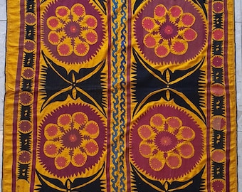 Könnte beinhalten: Ein großes, rechteckiges Textil mit einem sich wiederholenden Muster aus stilisierten Blumen in Rot-, Orange- und Gelbtönen. Die Blumen sind von schwarzen und blauen geometrischen Mustern umgeben. Das Textil ist aus einem gewebten Stoff gefertigt und hat eine raue Textur.