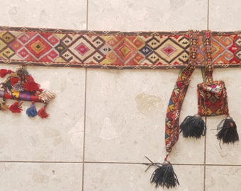 Op de afbeelding: Een kleurrijke, bedrukte textielen riem met een geometrisch ontwerp in rood, geel en bruin. De riem heeft een bijpassend zakje en kwastjes. Een apart decoratief stuk met kwastjes is ook inbegrepen.