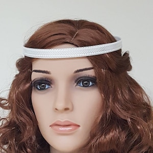 May include: A white headband with a delicate mesh pattern. The headband is worn on a mannequin with long, curly brown hair.