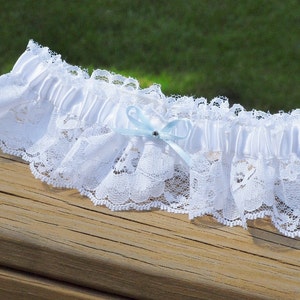 May include: White lace garter with a light blue satin bow and a rhinestone in the center.