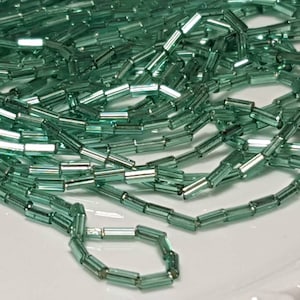 May include: A strand of light green glass beads, each bead is a rectangular tube with a slightly iridescent finish.