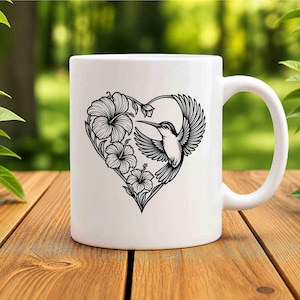 K&ouml;nnte beinhalten: Ein wei&szlig;er Keramikbecher mit einer schwarzen Strichzeichnung eines Kolibris und Hibiskusbl&uuml;ten, die in Herzform angeordnet sind. Das Motiv ist mittig auf der Vorderseite des Bechers platziert, der eine glatte Oberfl&auml;che und einen geschwungenen Henkel hat.