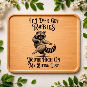 May include: A rectangular light brown wooden serving tray featuring a black graphic illustration of a dancing raccoon in the center. The text reads: If I Ever Get RABIES YOU'RE HIGH ON MY BITING LIST. The tray has rounded corners and raised edges.