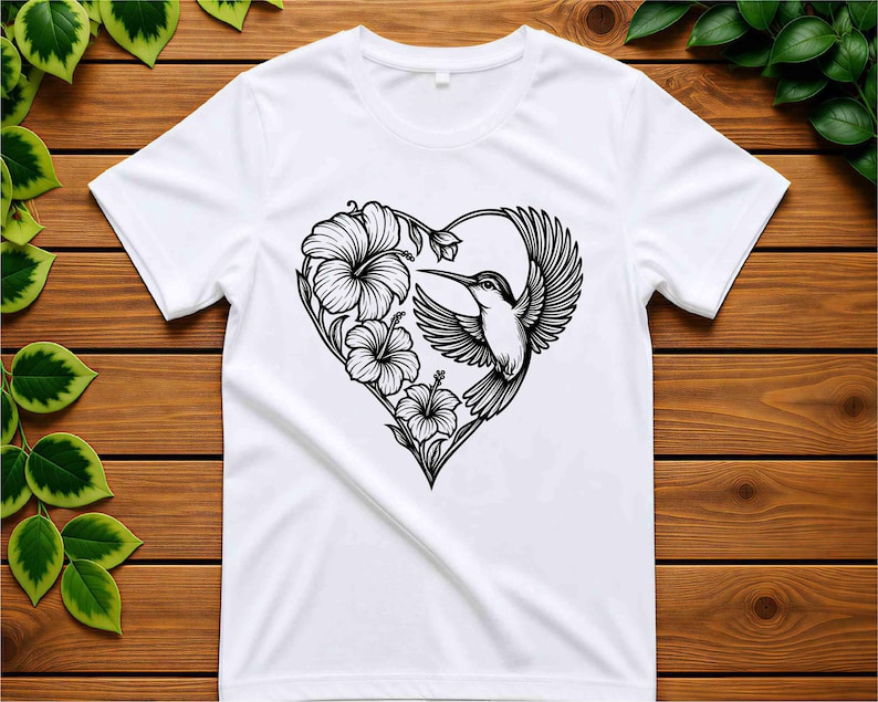 K&ouml;nnte beinhalten: Ein wei&szlig;es T-Shirt mit kurzen &Auml;rmeln und einer schwarzen Strichgrafik auf der Brust. Das Design zeigt einen fliegenden Kolibri zusammen mit drei Hibiskusbl&uuml;ten, die zusammen die Form eines Herzens bilden.