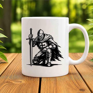 May include: A white ceramic mug featuring a black graphic illustration of a knight in full armour kneeling while holding a long sword upright. The knight wears a helmet and a cape, with a cross emblem visible on the chest plate of the armour.