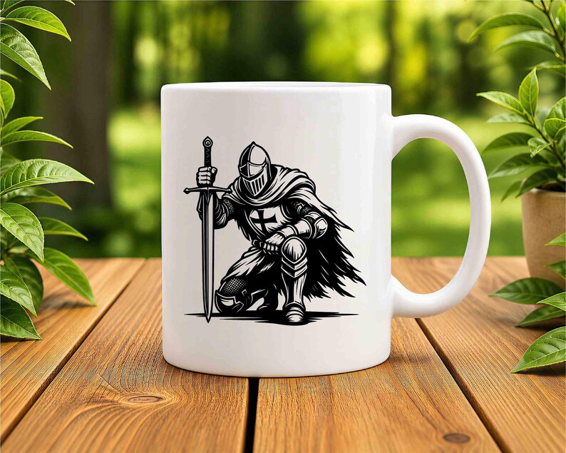 May include: A white ceramic mug featuring a black graphic illustration of a knight in full armour kneeling while holding a long sword upright. The knight wears a helmet and a cape, with a cross emblem visible on the chest plate of the armour.