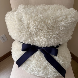 May include: A white fluffy throw blanket with a navy blue satin ribbon tied in a bow.