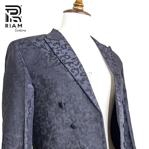 May include: A dark navy blue double-breasted blazer with a subtle floral pattern. The blazer is displayed on a mannequin and features two rows of buttons. The logo "RIAM Creations" is visible in the upper left corner.