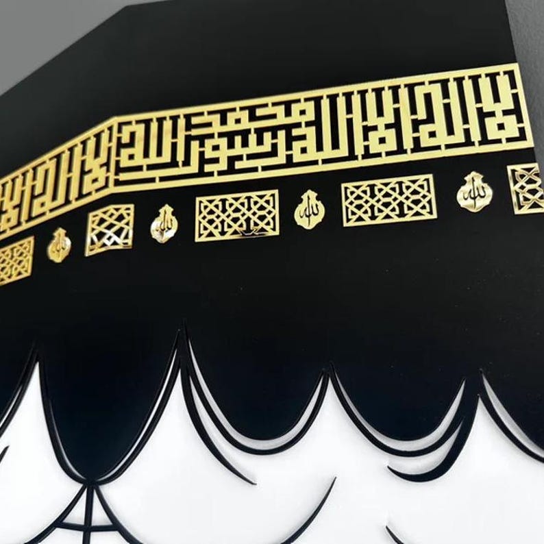 May include: A black and gold Islamic art wall decor featuring a stylised depiction of the Kaaba, the cubical building at the centre of Islam's holiest mosque in Mecca, Saudi Arabia. The Kaaba is surrounded by a gold Arabic inscription and decorative elements.