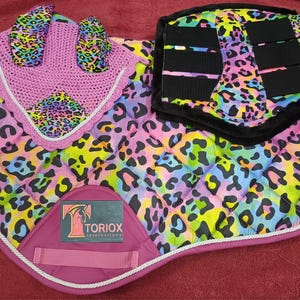 Puede incluir: Un conjunto de equitación con un estampado de leopardo vibrante en rosa, amarillo, azul y verde. El conjunto incluye una manta para la silla, una gorra para las orejas y vendas para las piernas. La manta para la silla tiene un diseño acolchado y un borde rosa.