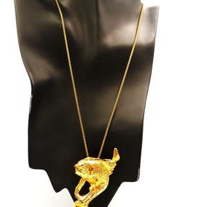 May include: A gold-colored fish pendant necklace displayed on a black mannequin. The fish pendant has detailed scales and fins, and is suspended from a delicate chain. The necklace is a statement piece, suitable for adding a touch of elegance.