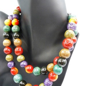 May include: A two-strand necklace with large, round beads in a variety of colors, including red, green, yellow, purple, and black. The beads are displayed on a black mannequin bust.
