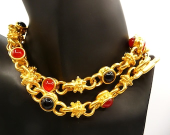 May include: A gold-tone chain necklace featuring alternating round red and black cabochon stones set within textured metal links. The necklace includes decorative cross-shaped spacers between the links and secures with a toggle clasp.