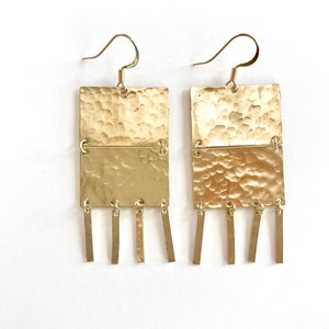 May include: A pair of gold-toned earrings. Each earring features a hammered rectangular top section, a smooth rectangular bottom section, and dangling rectangular bars. The earrings have a hook closure and are displayed against a white background.