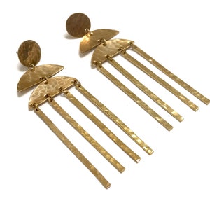 May include: A pair of gold-colored earrings with a hammered texture. Each earring features a circular stud, a half-circle shape, and several long, rectangular bars hanging down. The earrings are displayed against a white background.