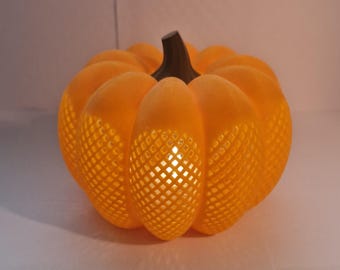 May include: Orange pumpkin-shaped decorative light with a textured surface and a dark brown stem. The pumpkin has a lattice-like pattern that allows light to shine through, creating a warm glow. A festive autumn decoration.