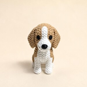May include: A small, three-dimensional printed figurine of a beagle dog. The figure features a textured, knitted-style surface pattern in tan and white. It has two round, black eyes and a black nose, with floppy ears and a seated posture.