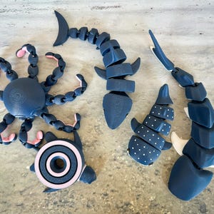 May include: Five articulated plastic sea creatures in black and white with pink accents. The creatures include a shark, an octopus, a whale shark, and two manta rays.