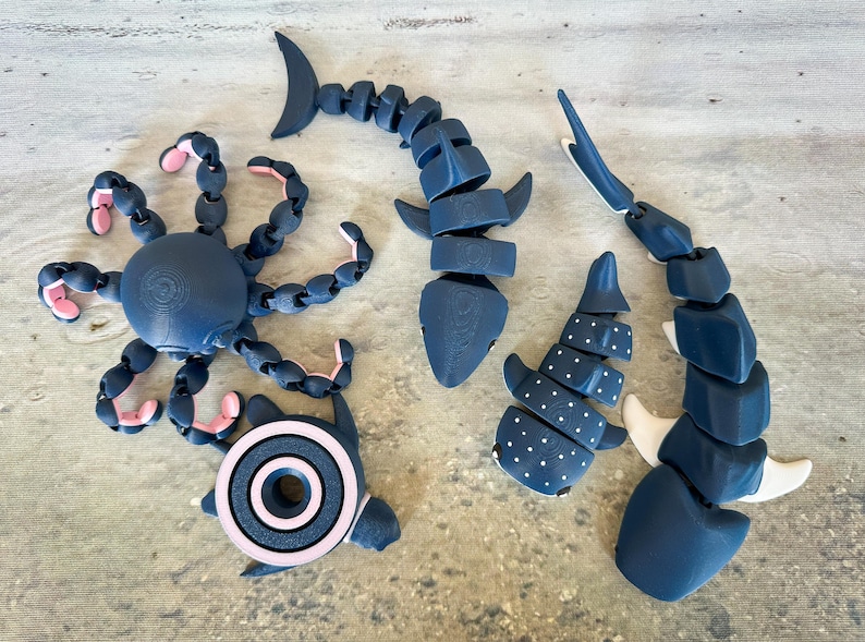 May include: Five articulated plastic sea creatures in black and white with pink accents. The creatures include a shark, an octopus, a whale shark, and two manta rays.