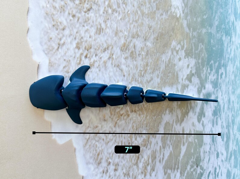 May include: A dark blue articulated shark toy, measuring 7 inches long. The toy is made of plastic and has a segmented body.