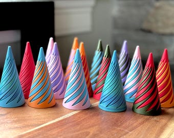 May include: A collection of 14 colourful cone-shaped ring holders with a swirling pattern. The holders are made of a smooth, hard material and are arranged in a row on a wooden surface.