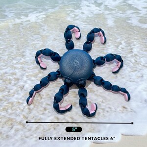 May include: A blue and pink octopus-shaped toy with flexible tentacles. The toy is 5 inches wide and has tentacles that extend to 6 inches long. The toy is on a sandy beach.