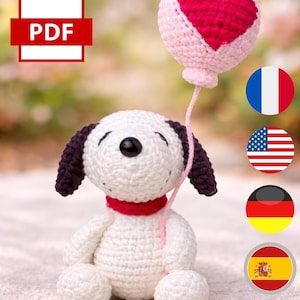 May include: A crocheted Snoopy-like character with a red collar and black ears, holding a pink balloon with a red heart. A PDF icon is in the upper left corner, with flags of France, the USA, Germany, and Spain.
