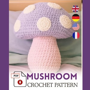 Peut inclure: Un coussin en crochet en forme de champignon, aux couleurs pastel. Le chapeau du champignon est lavande avec des taches blanches, et le pied est rose clair. Le texte "Mushroom Crochet Pattern" est inclus.