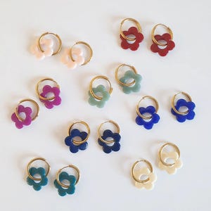 Peut inclure: Plusieurs boucles d'oreilles créoles en forme de fleur, de différentes couleurs : rose, rouge, vert, bleu et crème. Les boucles d'oreilles ont des cerceaux dorés, présentées sur fond blanc.