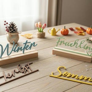 Peut inclure: Quatre enseignes décoratives en bois portant les mots allemands Winter, Fruehling, Herbst et Sommer en écriture cursive. Le signe Winter est bleu sur un socle en bois, Fruehling est vert sur un socle, tandis que Herbst et Sommer sont plats.