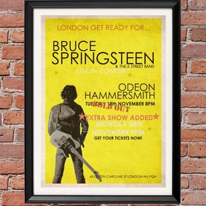 Puede incluir: Póster de concierto enmarcado para Bruce Springsteen & The E Street Band, con fondo amarillo y texto negro. El póster incluye una silueta de una persona con una guitarra y detalles del concierto en Londres.