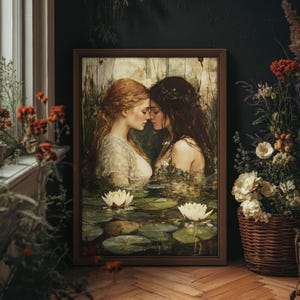 May include: A framed art print depicts two women embracing in a serene water scene with lily pads and flowers. One woman has auburn hair, the other dark hair. The artwork is in a wooden frame, set against a dark wall.