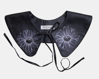 Könnte beinhalten: Schwarzer Kunstlederkragen mit weißem Augen- und Blumendesign. Der Kragen hat einen Bindeverschluss und der Text "VIZYA" ist auf der Rückseite sichtbar.