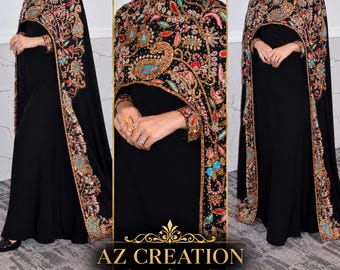 Puede incluir: Un vestido negro largo hasta el suelo con una capa de cuello alto adornada con intrincados bordados multicolores en tonos oro, turquesa, rosa y rojo. La prenda muestra el texto AZ CREATION en la parte inferior central.