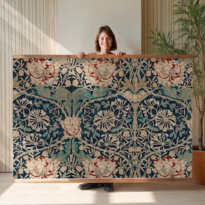 May include: A large, rectangular tapestry with a floral pattern in shades of navy blue, teal, cream, and red. The tapestry is framed in a light brown wooden frame. The floral design features stylized flowers and leaves.