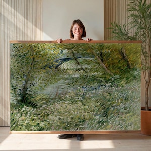 May include: A large framed print of a landscape painting featuring a bridge over a river, surrounded by lush green foliage. The artwork has a natural, impressionistic style with a wooden frame.