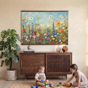 May include: A large floral painting with a wooden frame hangs above a wooden cabinet. A potted plant sits to the left. Two children play with toy cars and wooden blocks on a rug in front of the cabinet.