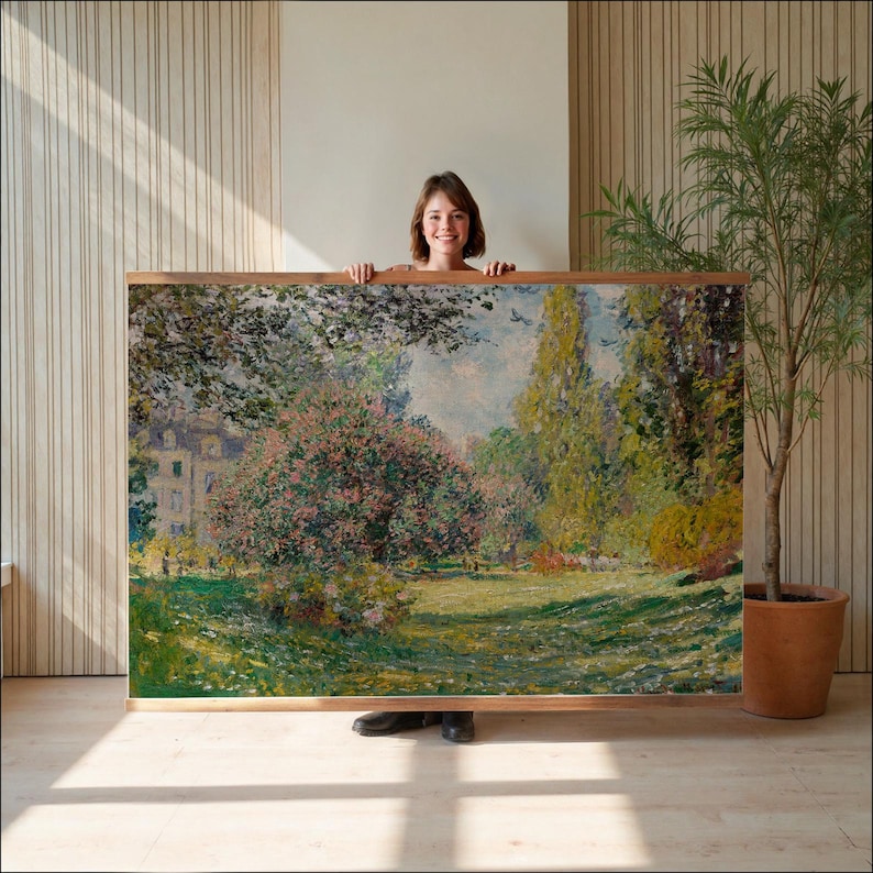 Pode incluir: Uma pintura de paisagem emoldurada com uma cena de parque com &aacute;rvores, um edif&iacute;cio e uma &aacute;rea gramada. A obra de arte tem uma moldura de madeira e &eacute; segurada por uma pessoa. A pintura tem uma paleta de cores naturais com tons verdes, rosa e azul.