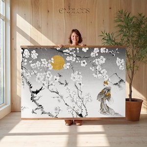 May include: A large wall art print featuring a Japanese-style illustration. The artwork depicts a geisha, cherry blossoms, a golden sun, and mountains in shades of gray, black, and white. The print is framed in a wooden border.