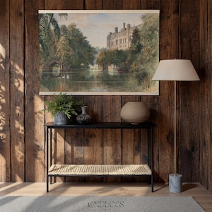 May include: A watercolour painting of a castle and lake is displayed above a black console table with a woven shelf. A floor lamp with a cream shade and a marble base stands to the right. Decorative vases and a potted plant are on the table.