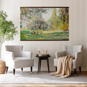 Pode incluir: Uma pintura de paisagem emoldurada retratando uma cena de parque com &aacute;rvores, grama e um edif&iacute;cio ao fundo. Duas poltronas cinzentas com pernas pretas e pontas douradas est&atilde;o em frente &agrave; pintura. Uma pequena mesa preta com velas e um cobertor bege completam a cena.