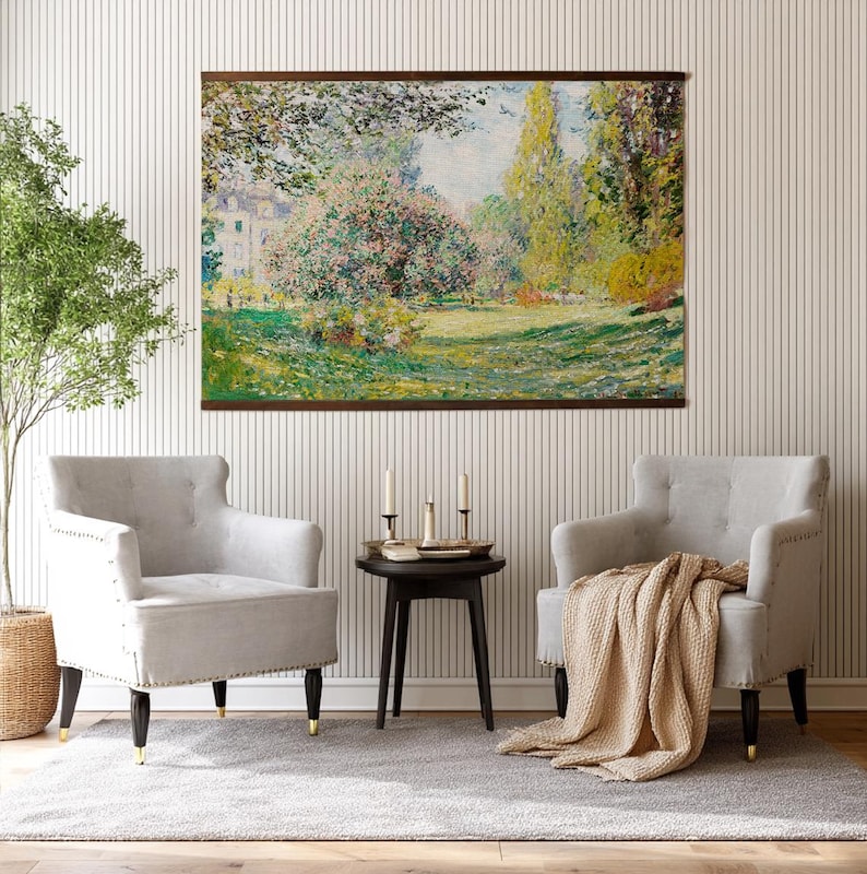 Pode incluir: Uma pintura de paisagem emoldurada retratando uma cena de parque com &aacute;rvores, grama e um edif&iacute;cio ao fundo. Duas poltronas cinzentas com pernas pretas e pontas douradas est&atilde;o em frente &agrave; pintura. Uma pequena mesa preta com velas e um cobertor bege completam a cena.