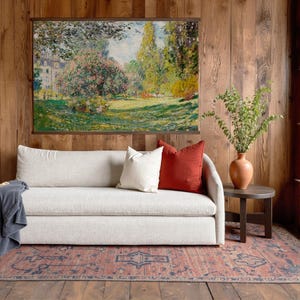 Pode incluir: Uma sala de estar com um sof&aacute; de cor clara adornado com almofadas brancas e cor de ferrugem. Uma pintura de paisagem emoldurada est&aacute; pendurada acima do sof&aacute;. Um vaso de terracota com vegeta&ccedil;&atilde;o est&aacute; em uma pequena mesa lateral. Um tapete estampado e pain&eacute;is de madeira completam a decora&ccedil;&atilde;o.