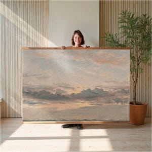 May include: A large framed artwork featuring a landscape painting of a cloudy sky with shades of gray, blue, and peach. The artwork is displayed against a light-colored wall, with a wooden frame.