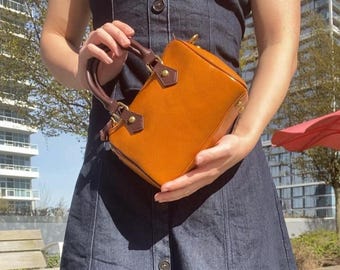 May include: A small, orange leather handbag with brown trim and gold hardware. The bag has a top handle and a shoulder strap.